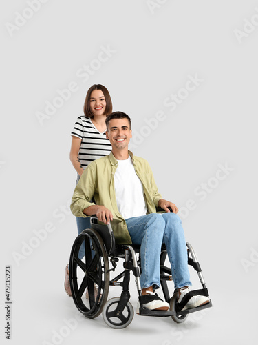 Young man in wheelchair and his wife on light background