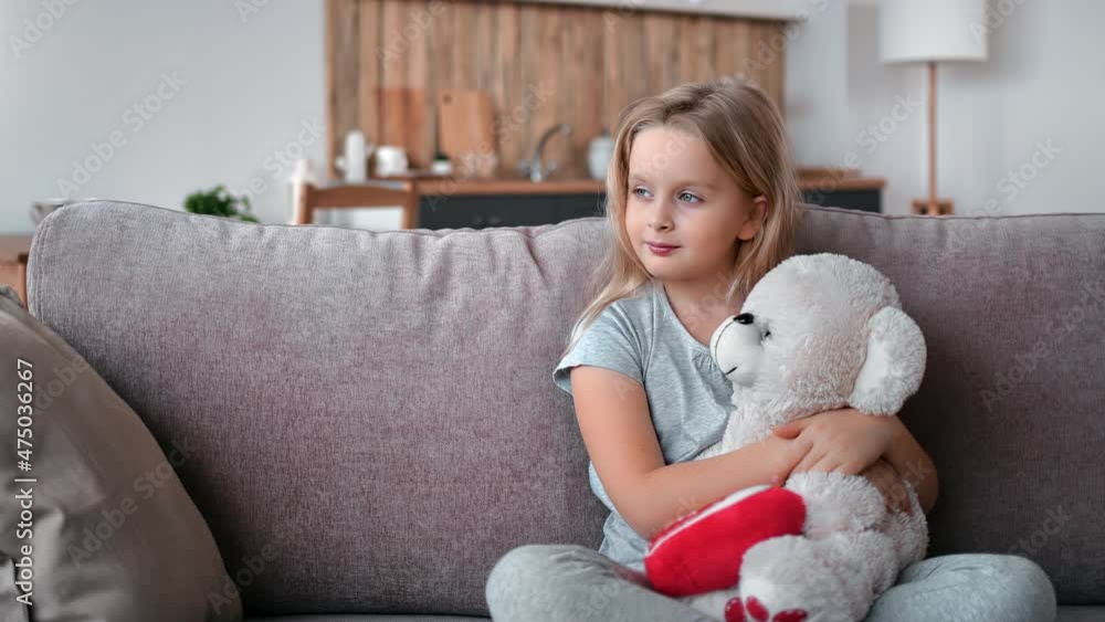 Smiling cute baby girl relaxing on comfortable couch hugging teddy bear feeling love friendship Smiling cute baby girl relaxing on comfortable couch hugging teddy bear feeling love friendship