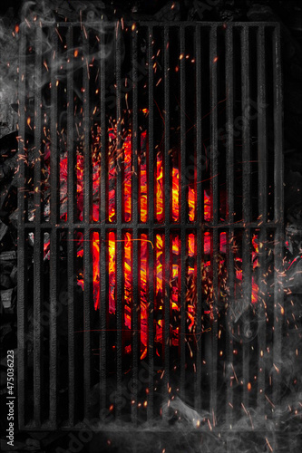 Top view through black barbecue grate of burning coals with sparks and white smoke