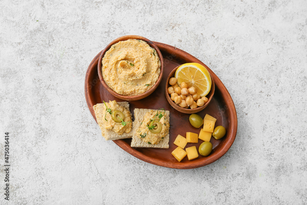 Bowl with delicious hummus, cheese, olives and crackers on light background