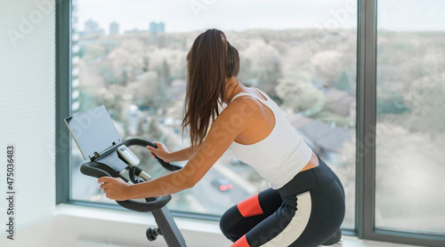 Home fitness workout woman training cardio on bike cyle with online gym class streaming. Girl biking on stationary bicycle indoor. photo