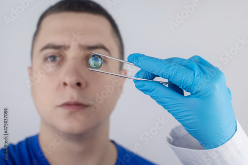 Conceptual shot of an eye crystalline lens replacement. Ophthalmic surgery. Return of sight. Removal of cataracts. Surgical intervention in the eyeball. Doctor holds the implant near the patient