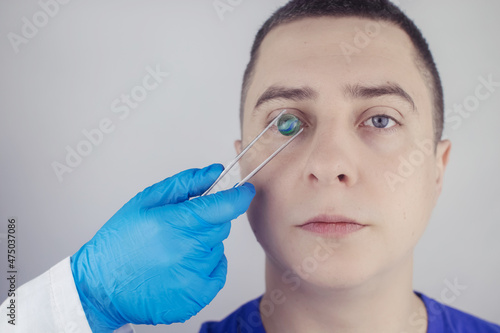 Fototapeta Naklejka Na Ścianę i Meble -  Conceptual shot of an eye crystalline lens replacement. Ophthalmic surgery. Return of sight. Removal of cataracts. Surgical intervention in the eyeball. Doctor holds the implant near the patient