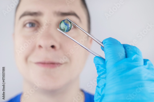 Conceptual shot of an eye crystalline lens replacement. Ophthalmic surgery. Return of sight. Removal of cataracts. Surgical intervention in the eyeball. Doctor holds the implant near the patient