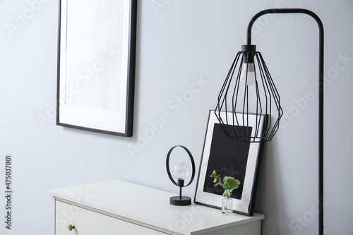 Frame, eucalyptus branches and lamp on shelf near light wall © Pixel-Shot