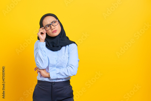 Portrait of pensive young Asian woman looking seriously thinking about a question isolated on yellow background © Sewupari Studio