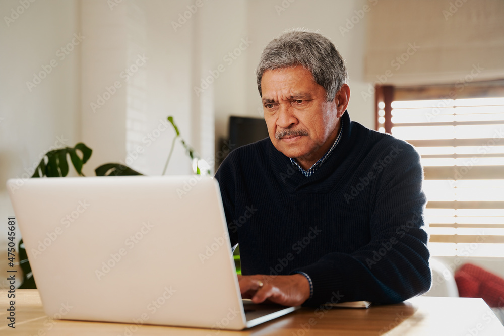 Concerned Multi-cultural elderly male reading news on laptop. Isolating in modern home, sitting at kitchen counter top. Concerned Multi-cultural elderly male reading news on laptop. Isolating in modern home, sitting at kitchen counter top.