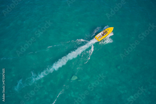 Boat performance fast movement on clear water aerial view. Yellow high-speed luxury boat with people moving on turquoise water. © Berg