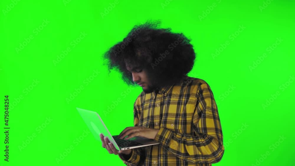 A young man with an African hairstyle on a green background is typing on a laptop. On a colored background A young man with an African hairstyle on a green background is typing on a laptop. On a colored background