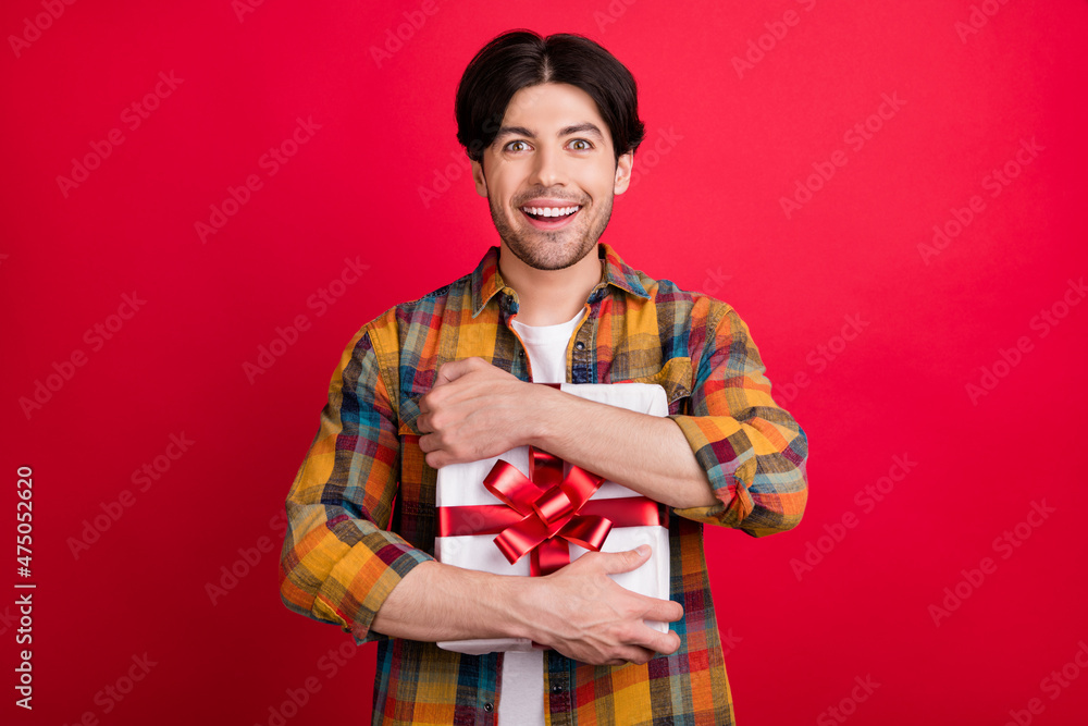 Photo of excited funny young gentleman wear plaid outfit smiling hugging present box isolated red color background Photo of excited funny young gentleman wear plaid outfit smiling hugging present box isolated red color background