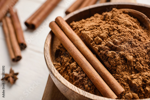 Foto Bowl with cinnamon powder and sticks on white wooden background, closeup