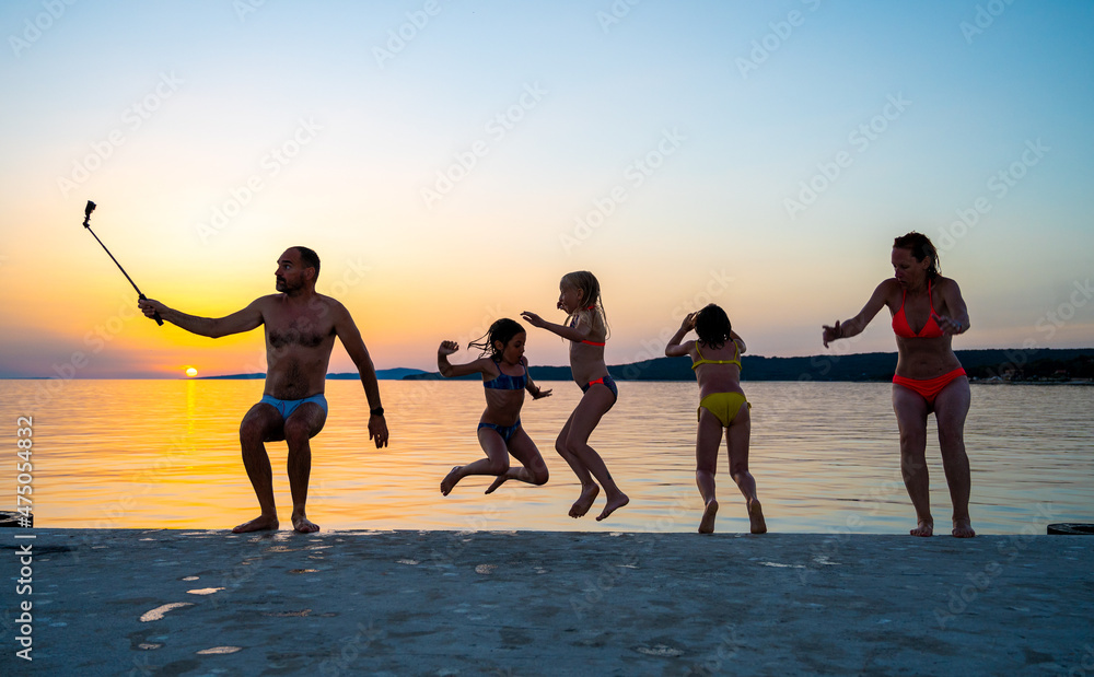 Fototapeta premium Family jumping from pier in the water at sunset.