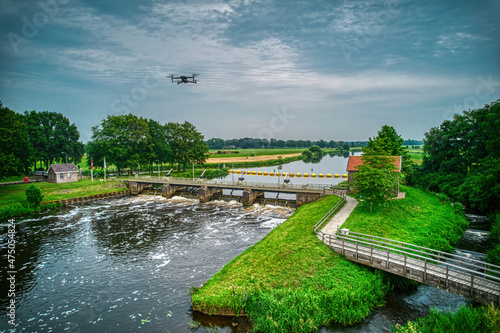 An aerial view with a flying drone in the background above a weir in the river Vecht. Lock keepers house next to the bridge. Fish pass, fish ladder. Overijssel Vecht