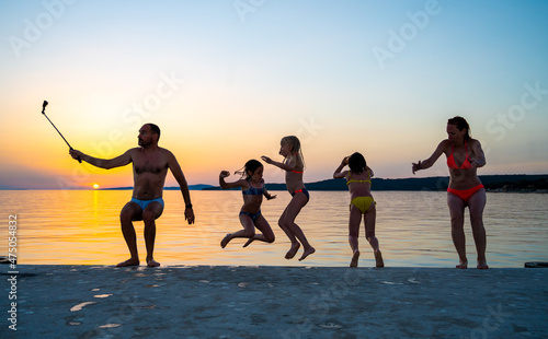 Family jumping from pier in the water at sunset.