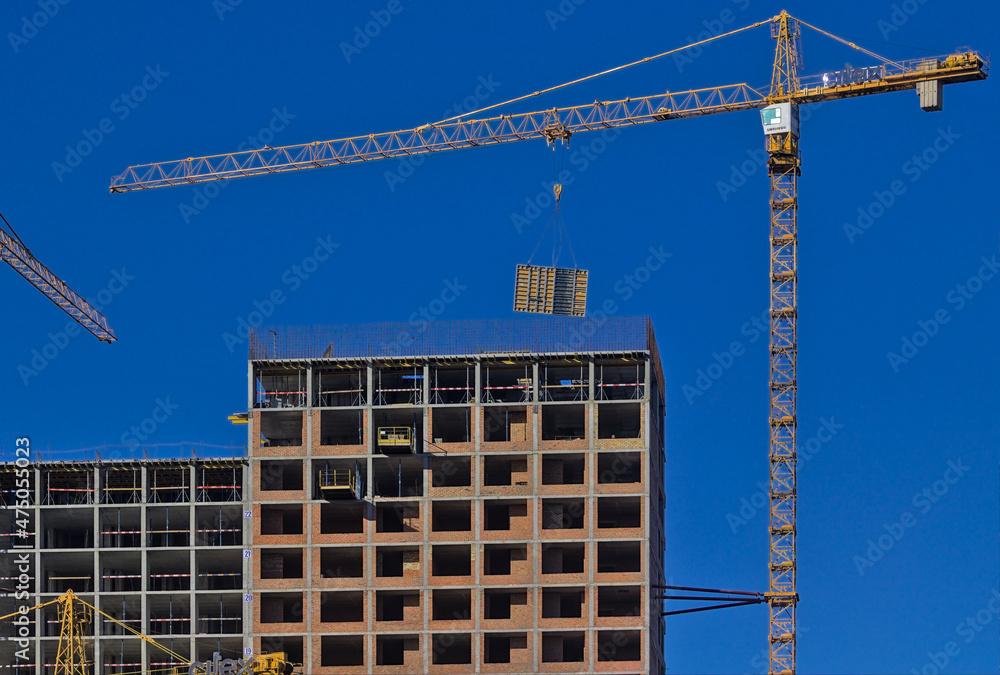 Fototapeta premium Kyiv, Ukraine - On the top floor of the new building under construction, large-sized structures are installed using a crane. Construction of a modern residential complex. Blue sky.