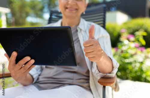 technology, old age and people concept - close up of happy smiling senior woman with tablet pc computer resting at summer garden and showing thumbs up