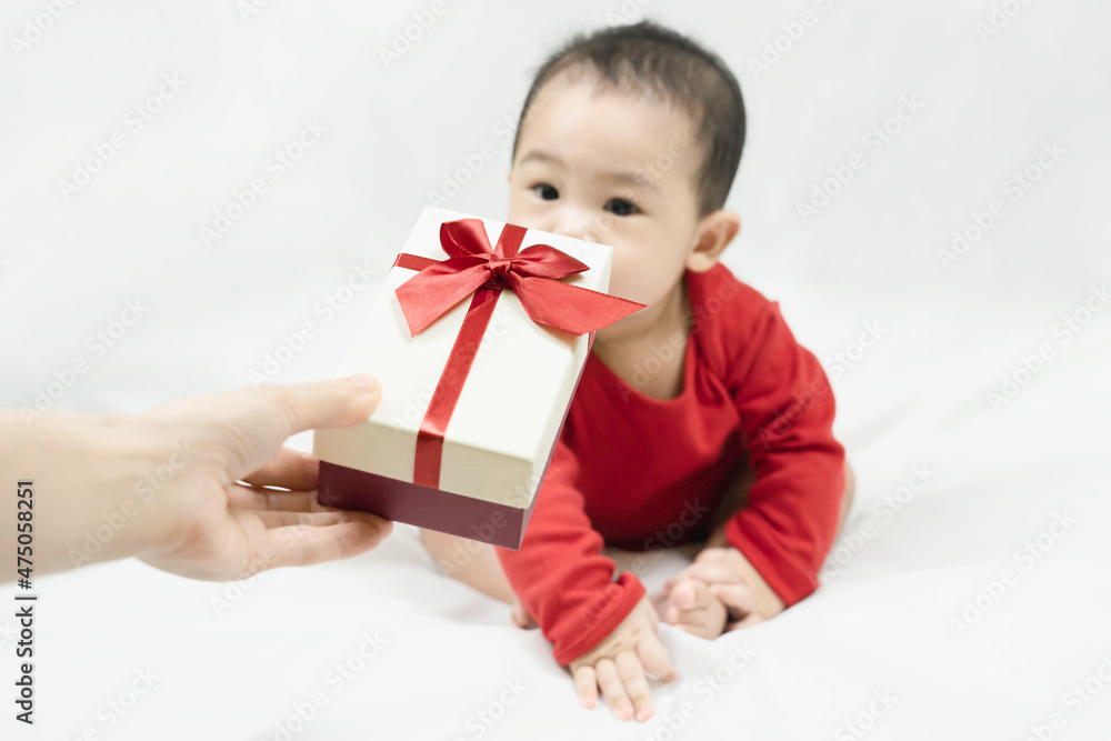 Cute asian baby in red bodysuit get gift box sitting on white blanket at home.Give Year present to child,kid,toddler.Concept holiday Christmas, happy new year, infants, childhood.selective focus. Cute asian baby in red bodysuit get gift box sitting on white blanket at home.Give Year present to child,kid,toddler.Concept holiday Christmas, happy new year, infants, childhood.selective focus.