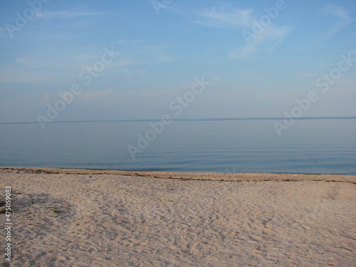 Panorama of the sandy beach near the crystal clear waters of the calm sea on a background of barely cloudy evening sky.