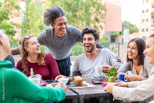 group of multiethnic friends having breakfast with coffee, cappuccino and chocolate muffin, meeting of young people outdoors at a coffee shop