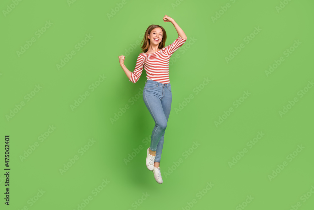 Photo of champion lady jump raise fists rejoice goal achievement wear striped shirt jeans isolated green color background