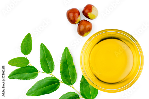 Bowl with jojoba oil, ripe fruits and green leaves on white background