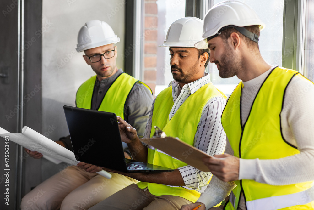 architecture, construction business and people concept - group of male architects in helmets with laptop, blueprint and clipboard working at office architecture, construction business and people concept - group of male architects in helmets with laptop, blueprint and clipboard working at office