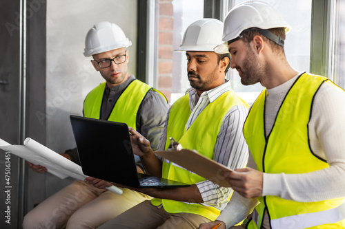 architecture, construction business and people concept - group of male architects in helmets with laptop, blueprint and clipboard working at office