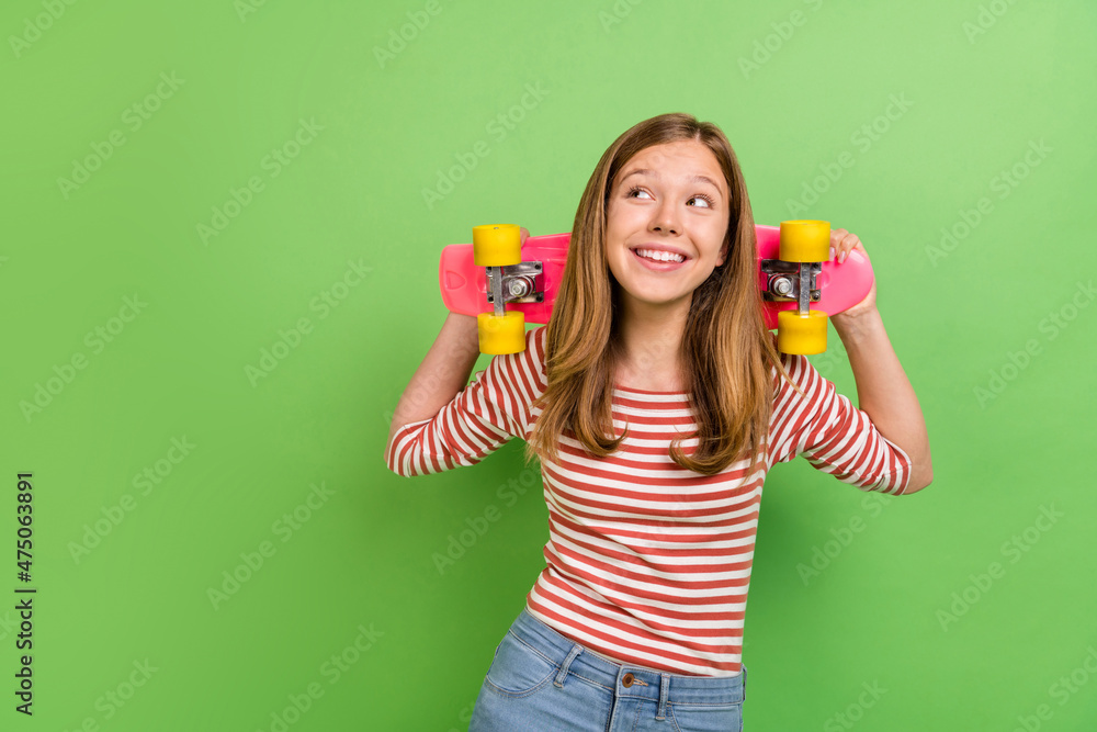 Photo of funny teen dreamy lady hold skateboard look empty space wear striped shirt isolated green color background Photo of funny teen dreamy lady hold skateboard look empty space wear striped shirt isolated green color background