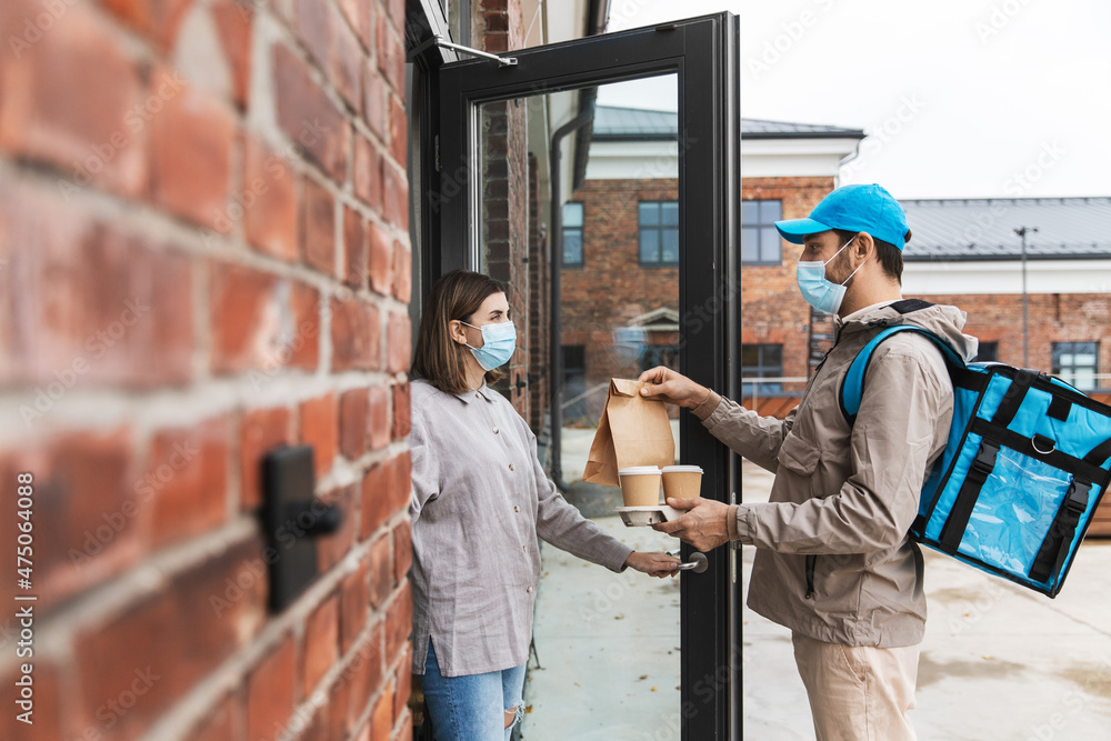 food shipping, pandemic and people concept - delivery man in mask with thermal insulated bag giving order and coffee to female customer at home food shipping, pandemic and people concept - delivery man in mask with thermal insulated bag giving order and coffee to female customer at home