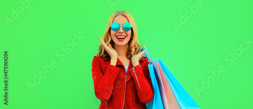 Colorful portrait of stylish happy smiling young woman with shopping bags posing wearing red jacket on green background