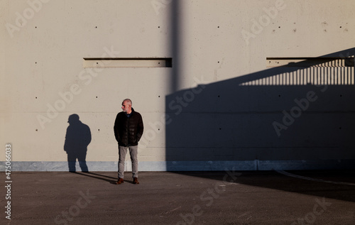Full length of adult man in winter clothes standing against white wall with sunlight and shadow