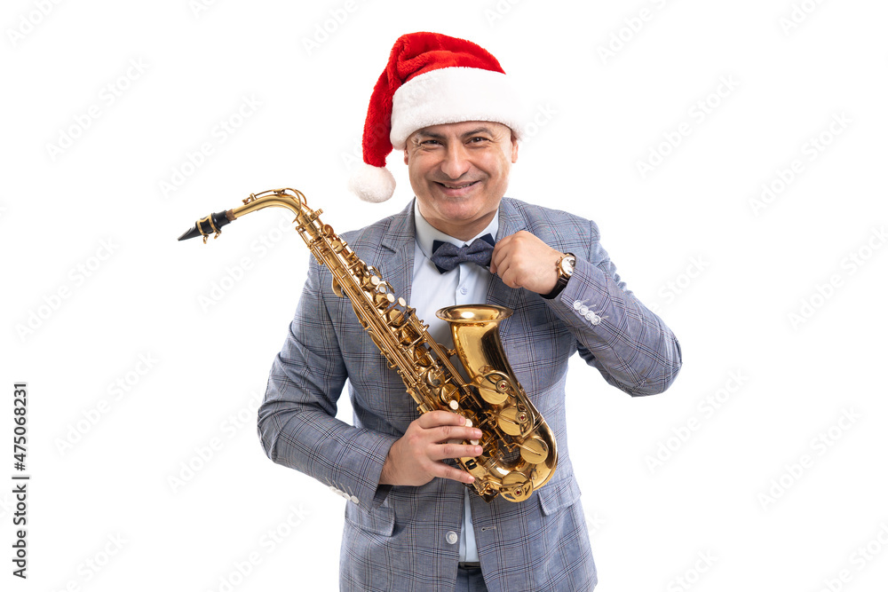 Fototapeta premium Funny musician wears in Santa's hat holds saxophone while straightening bow tie on studio background