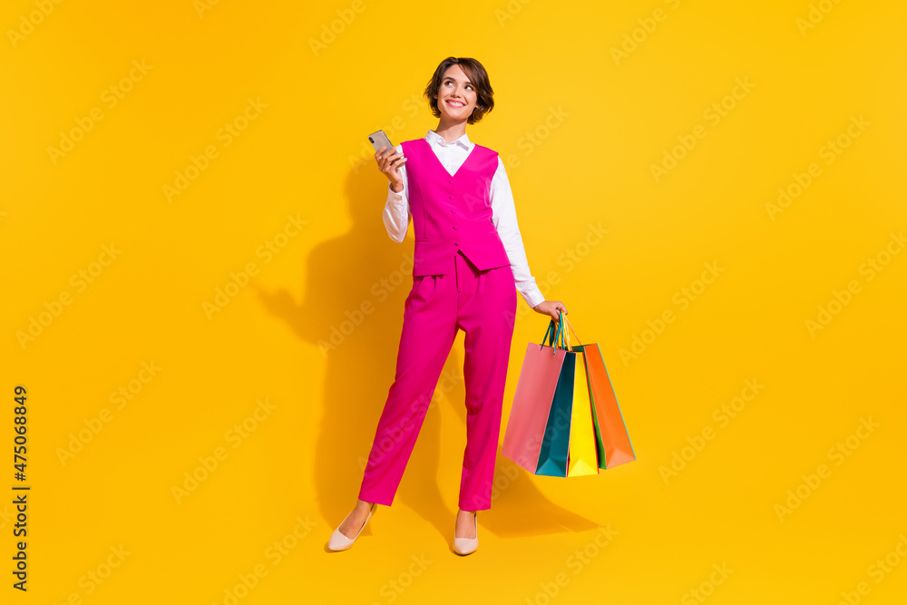 Photo of dreamy sweet young woman dressed pink suit holding shoppers modern gadget looking empty space isolated yellow color background Photo of dreamy sweet young woman dressed pink suit holding shoppers modern gadget looking empty space isolated yellow color background