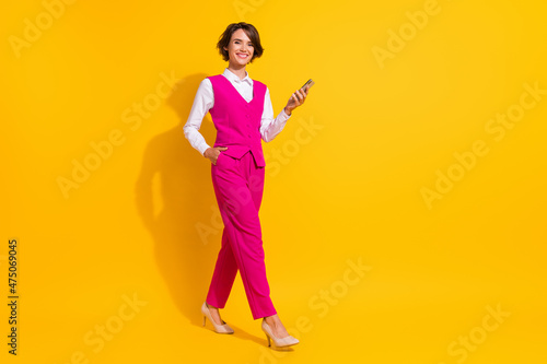 Photo of charming shiny young lady wear pink suit smiling walking typing modern device empty space isolated yellow color background © deagreez
