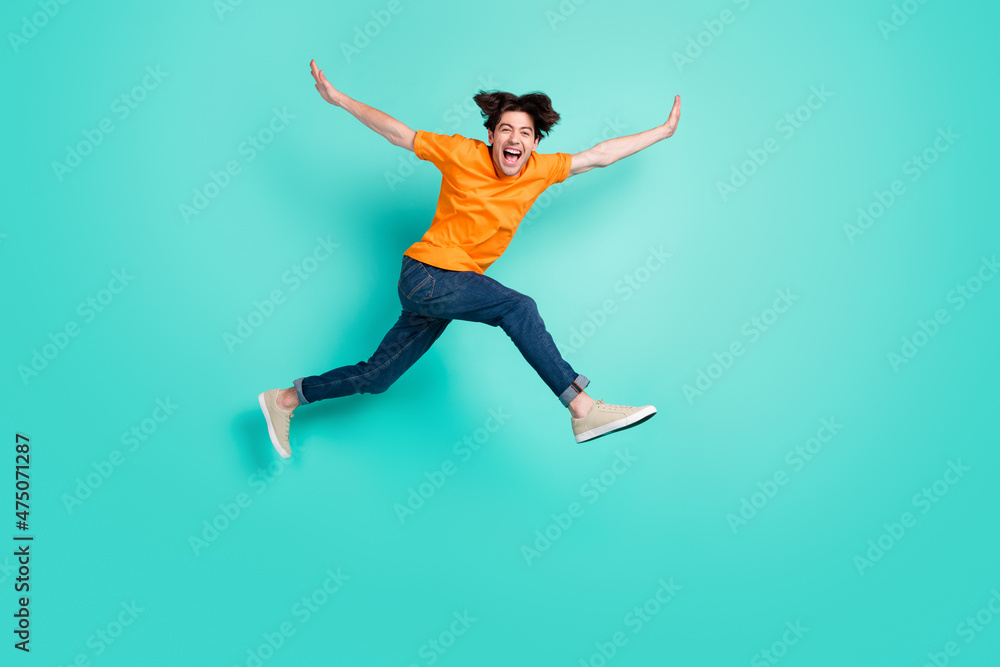 Full size photo of cool brown hair young guy jump yell wear t-shirt jeans sneakers isolated on blue background