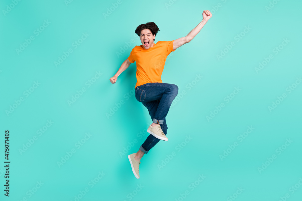 Full size photo of funny brown hair millennial guy jump wear t-shirt jeans sneakers isolated on blue background Full size photo of funny brown hair millennial guy jump wear t-shirt jeans sneakers isolated on blue background