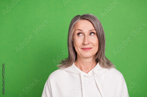 Photo of dreamy pretty old woman dressed white sweatshirt smiling looking empty space isolated green color background