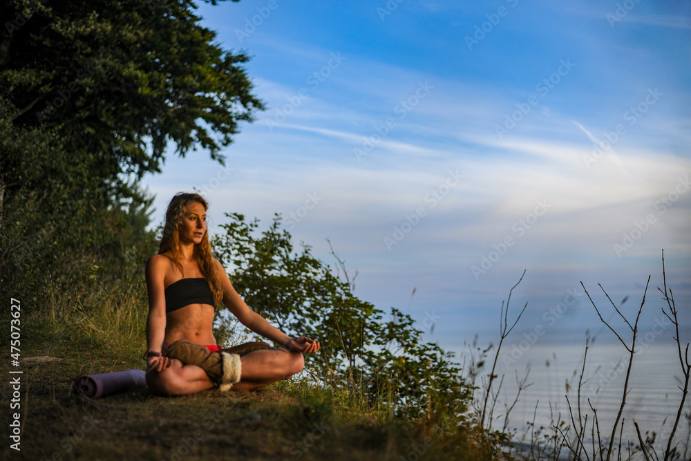 junge Frau sitzt in der Natur und meditiert im Schneidersitz