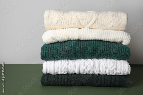 Stack of stylish knitted sweaters on green table against grey background © Pixel-Shot