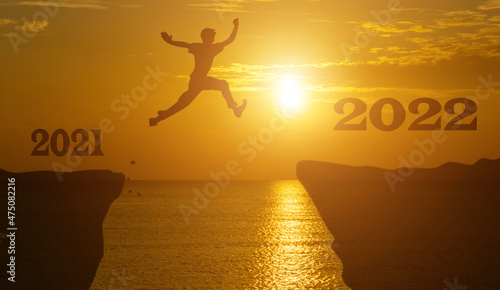 Silhouette man jump between 2021 and 2022 years with sunset background.