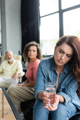 frustrated woman holding glass of water near african american girlfriend and psychologist on blurred background © LIGHTFIELD STUDIOS