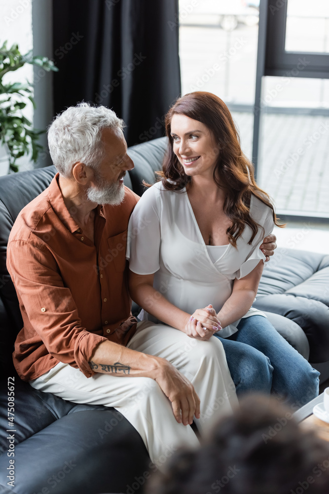 happy couple looking at each other while sitting on couch during psychological consultation