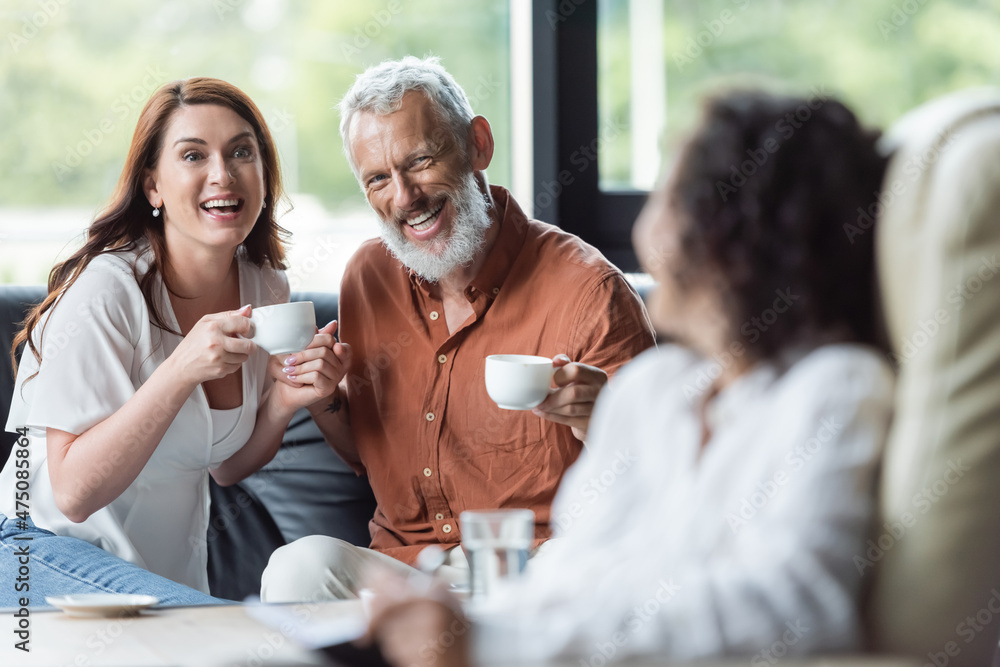 smiling couple sitting with coffee cups near blurred african american psychologist smiling couple sitting with coffee cups near blurred african american psychologist