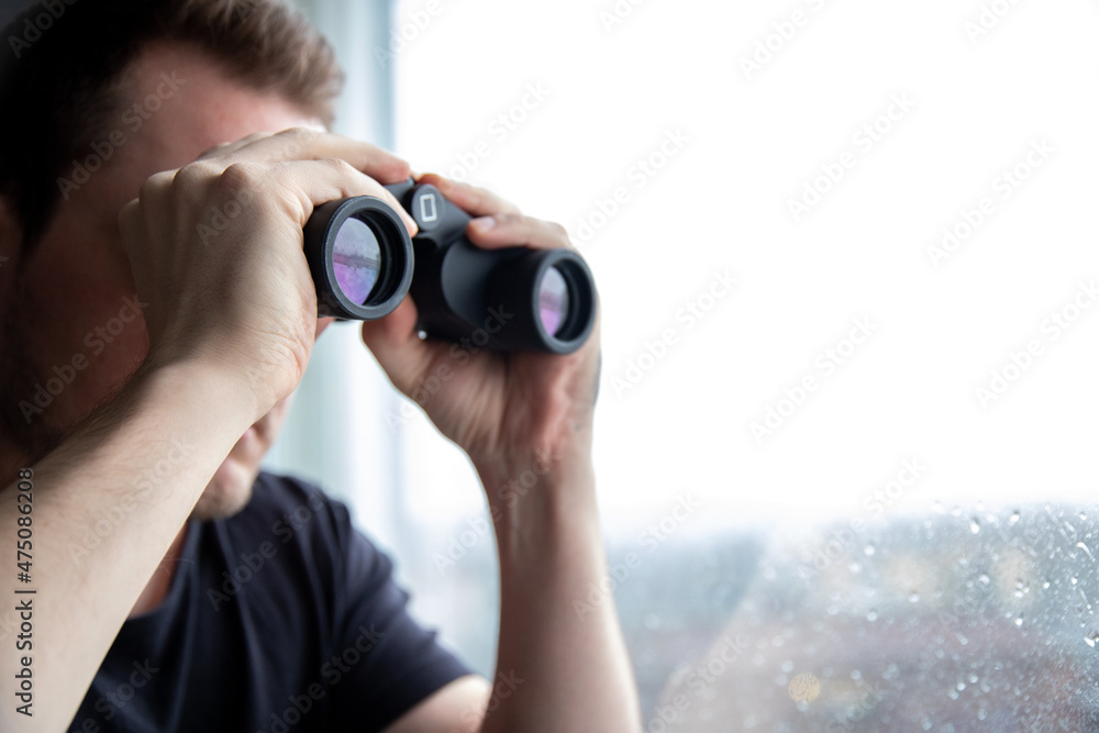 Man watching outside through his window with pair of binoculars. Man watching outside through his window with pair of binoculars.