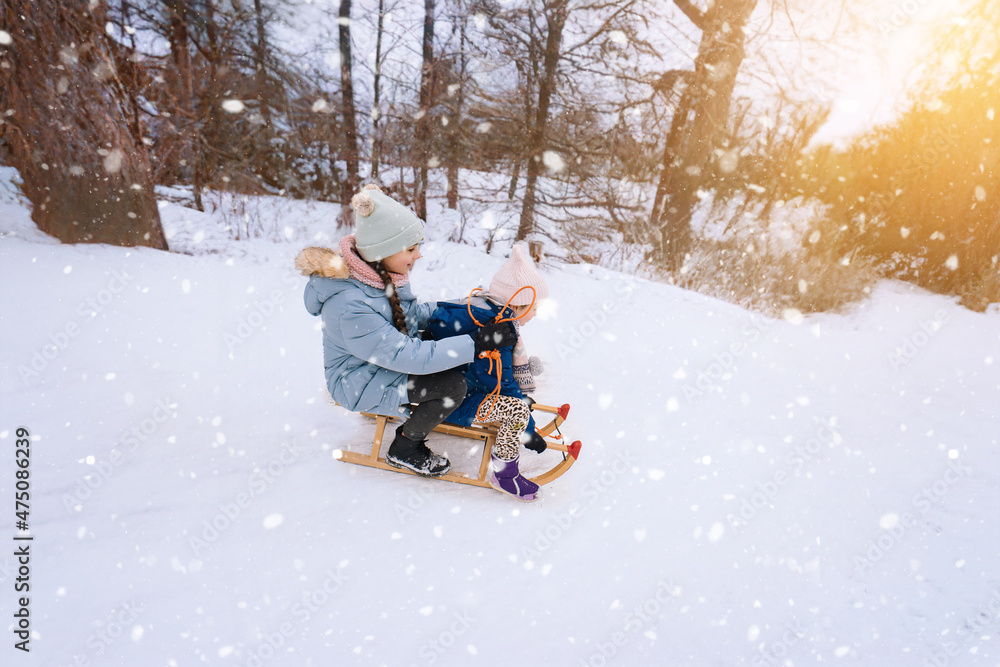 Two children ride on wooden retro sled on sunny winter day. Active winter outdoors games. Winter activities for kids. Children playing with snow in park. Happy Christmas vacation concept