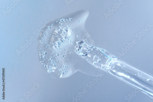 Pipette with fluid hyaluronic acid on blue background. Cosmetics and healthcare concept closeup. Dose of serum or retinol with air bubbles. Flat lay. Luxury gel or beauty product presentation in macro