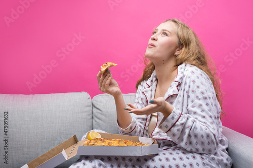 The girl sits on the sofa and eats pizza.