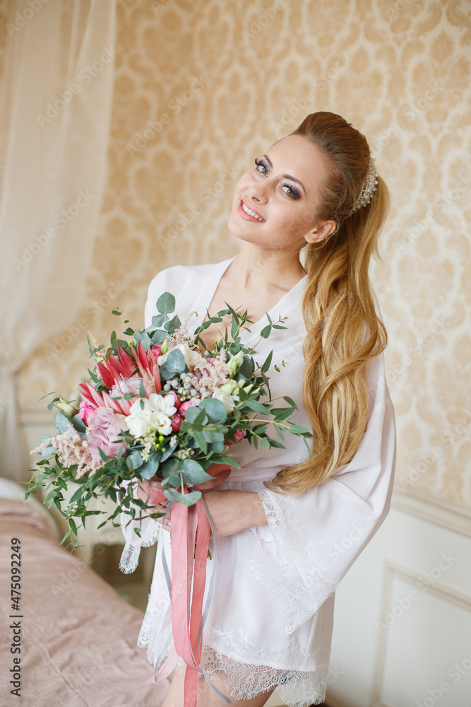 Pretty young Bride. Blonde-haired woman with wedding hair-style with a long tail. Boudoir morning of the bride. Looking on her bouquet