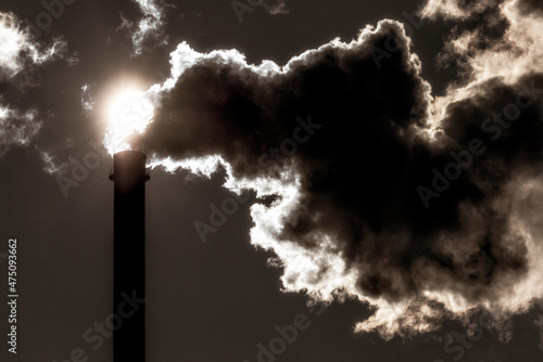 Dark smoke from chimney against the sun on sky