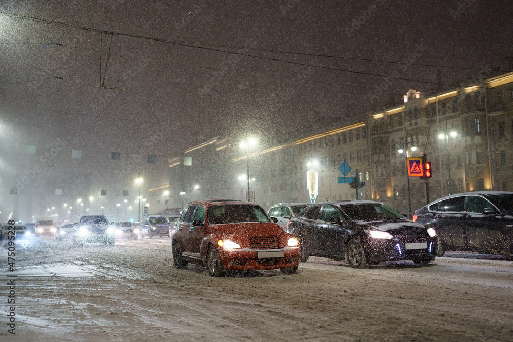 Heavy snowfall paralyzes city traffic, snowy road with many cars stacked in jam during snow blizzard at night, traffic collapse on winter highway. Driving in bad weather and low visibility Heavy snowfall paralyzes city traffic, snowy road with many cars stacked in jam during snow blizzard at night, traffic collapse on winter highway. Driving in bad weather and low visibility